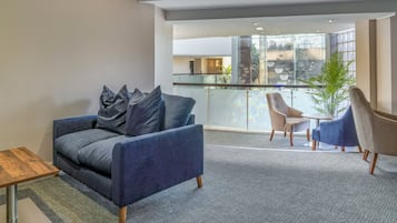 A modern living room with a grey sofa, a small wooden table, and a balcony with a glass railing.