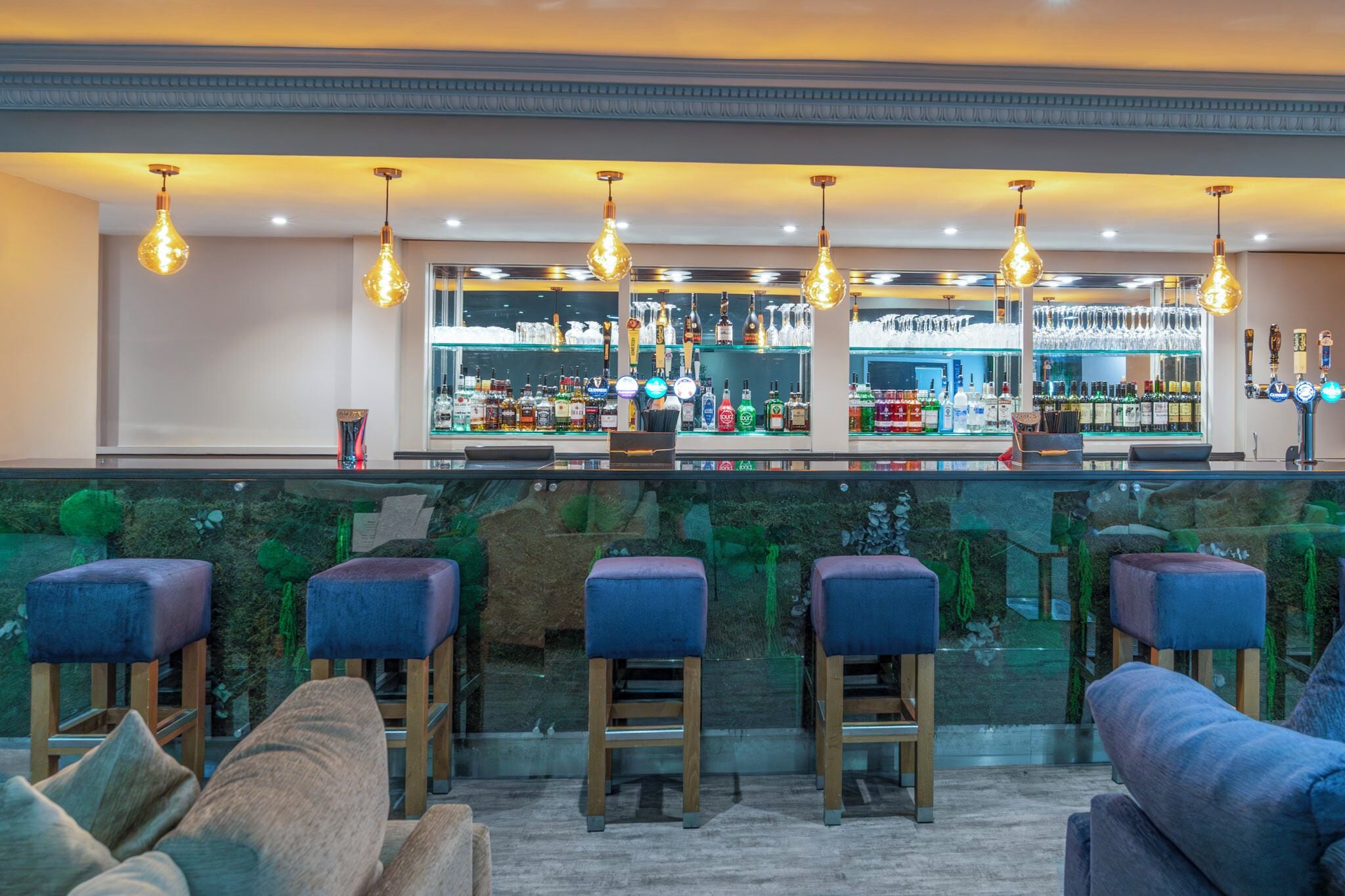 A bar area with stools, a counter with bottles, and hanging light fixtures.