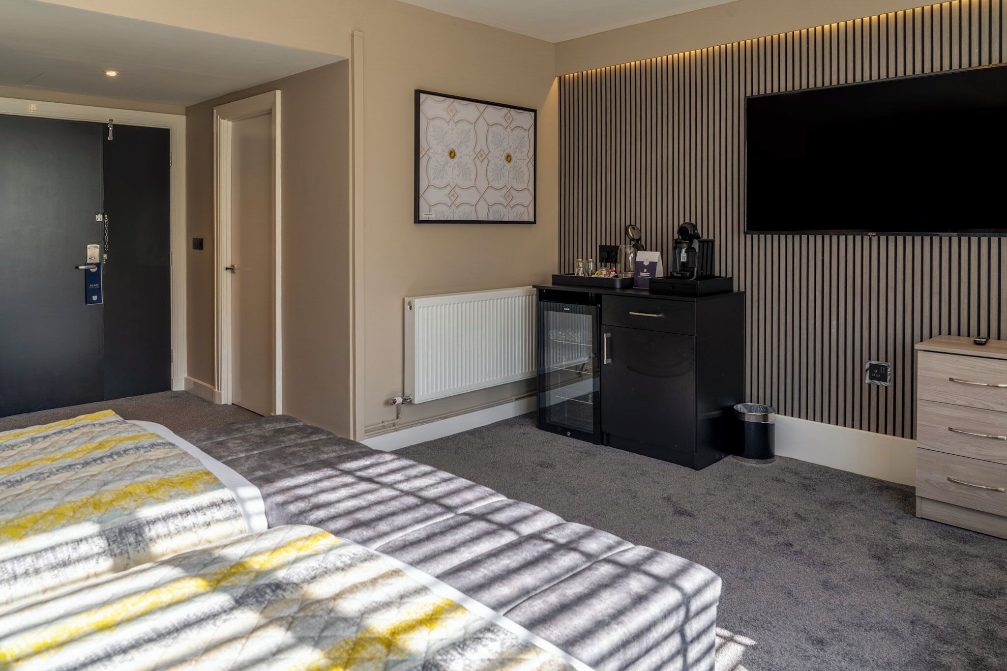 Una habitación de hotel moderna con cama, televisión, kitchenette pequeña y radiador.