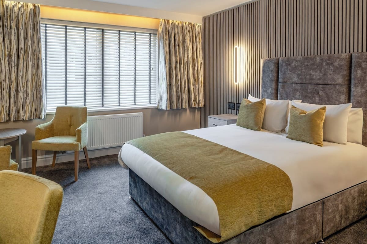 Une chambre d’hôtel moderne avec un grand lit, un coin salon avec des fauteuils et une fenêtre avec des rideaux.