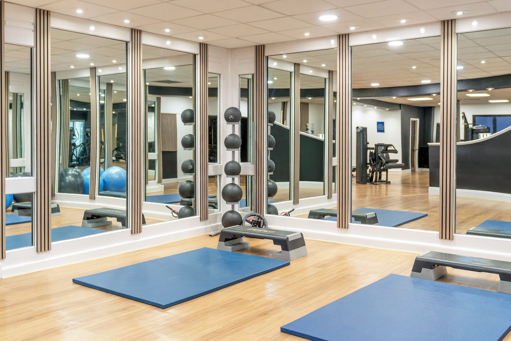 A gym with exercise equipment, mirrored walls, and blue mats.