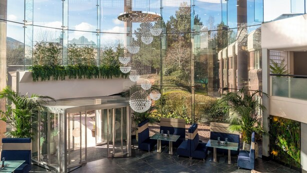 A modern indoor space with glass walls, seating areas, and hanging decorative lights.