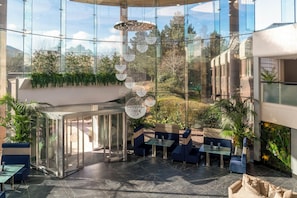 Espaço interior moderno com paredes de vidro, áreas de estar e luminárias decorativas penduradas.