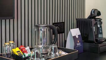 A coffee station with a coffee maker, a glass carafe, and a tray with coffee pods and glasses.