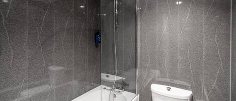 A modern bathroom with a glass-enclosed shower, a white bathtub, and a toilet.