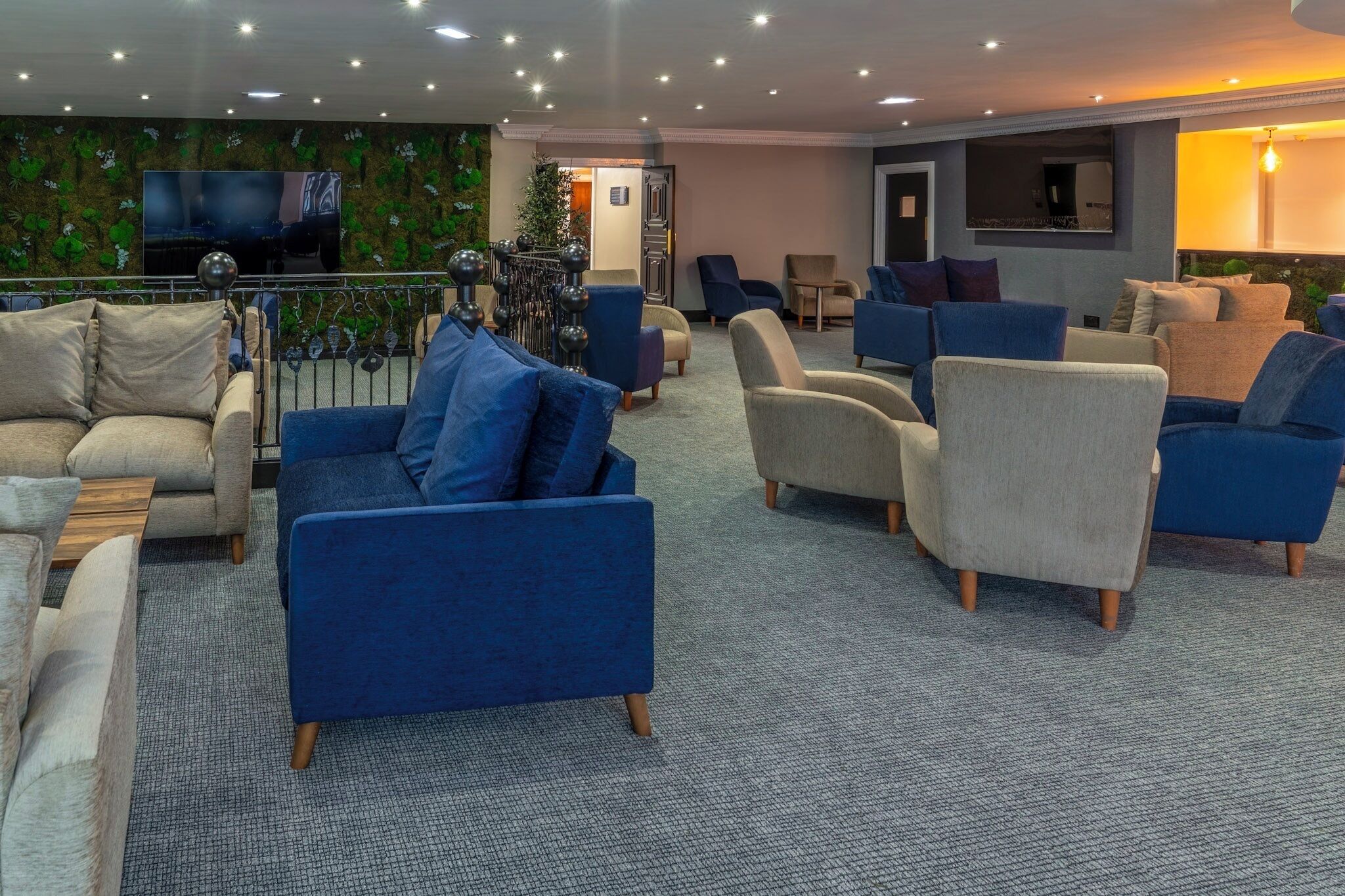 A modern lounge area with sofas and armchairs, a flat-screen TV, and a decorative wall.