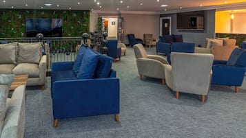 A modern lounge area with sofas and armchairs, a flat-screen TV, and a decorative wall.