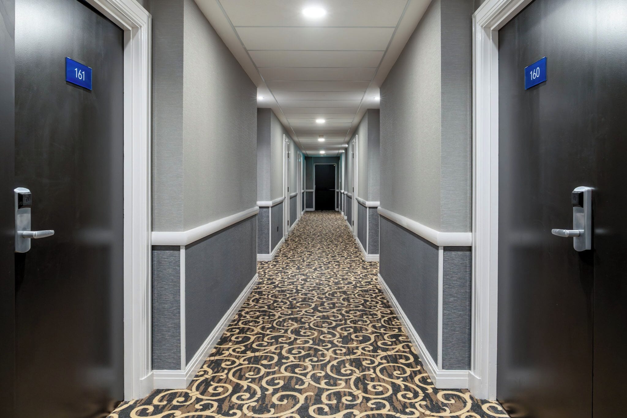 A hallway with doors numbered 161 and 160, carpeted with a patterned design, and white-framed doors.