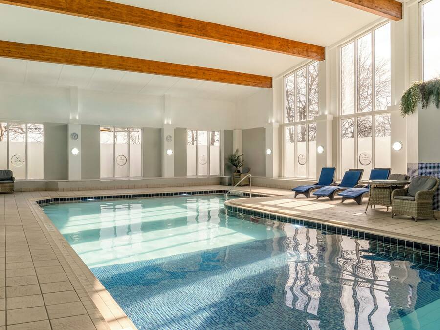 An indoor swimming pool with lounge chairs and wicker furniture.
