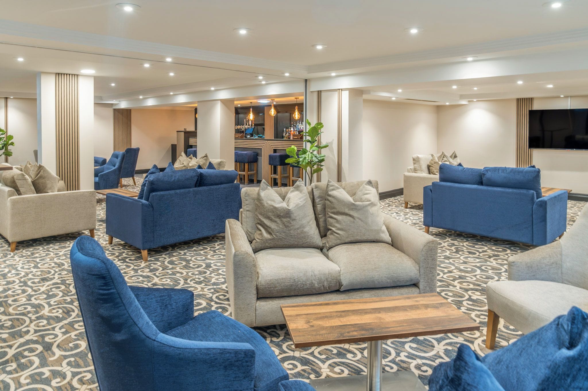 A hotel lobby with multiple seating areas, a bar, and a television screen.