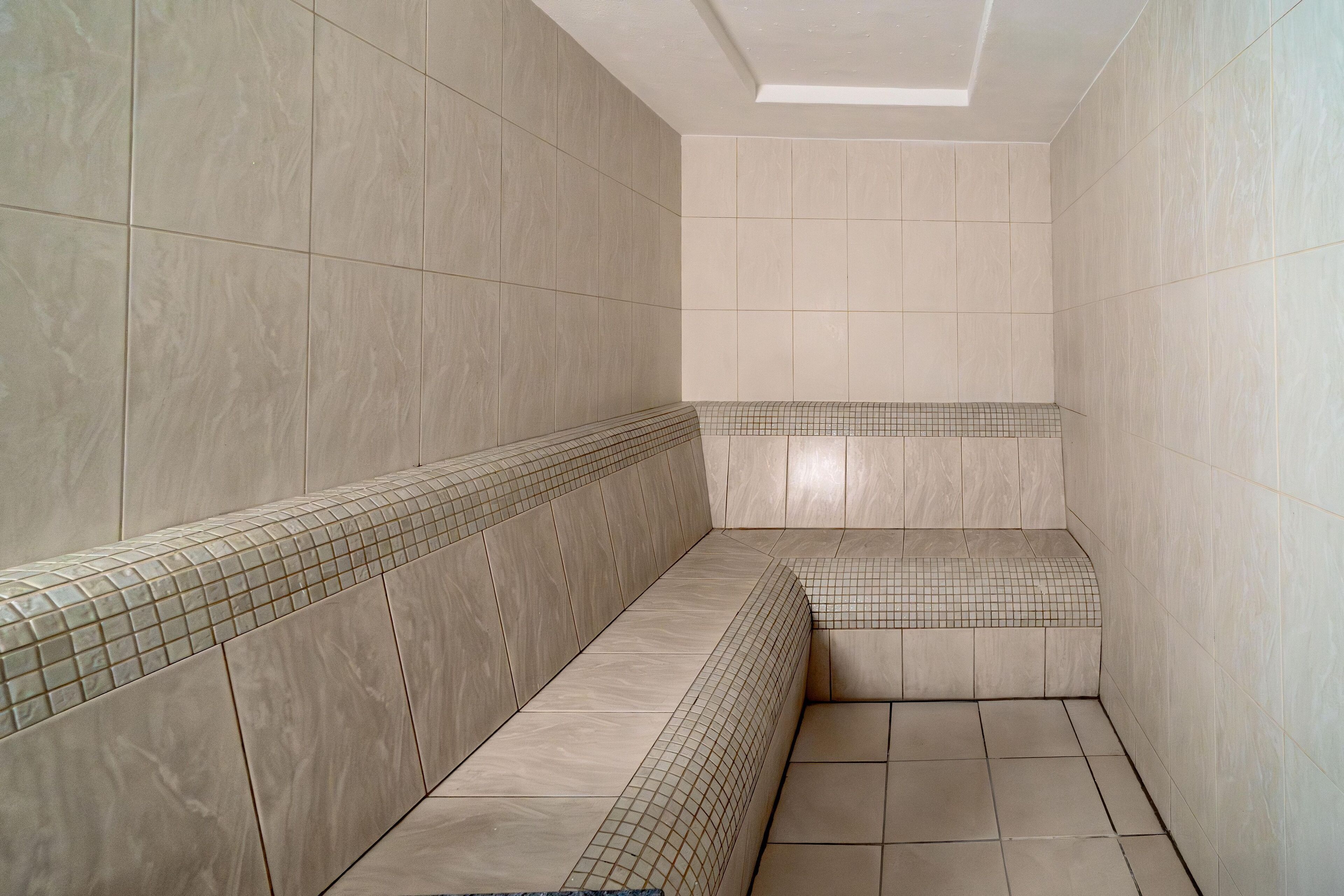 Un baño con paredes y suelo de baldosas color beige, un banco y un tragaluz.