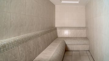 Un baño con paredes y suelo de baldosas color beige, un banco y un tragaluz.