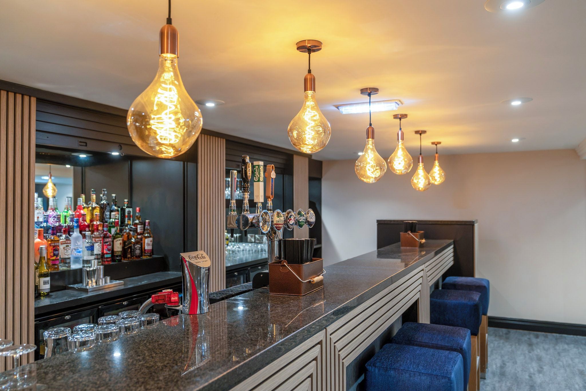 A bar area with a long counter, multiple taps, and hanging light fixtures.