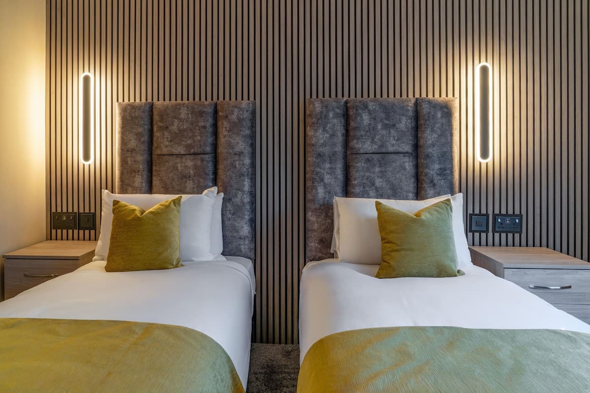 Une chambre d’hôtel avec deux lits, un mur en lambris de bois et des luminaires modernes.