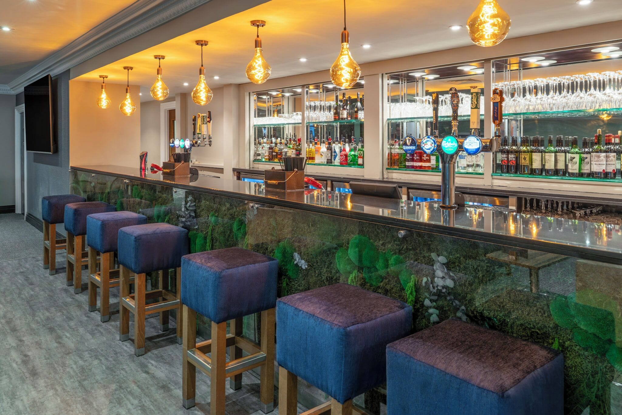 A bar area with stools, a bar counter, and shelves of bottles.