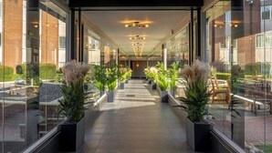 A corridor with potted plants, a glass wall, and a view of the outside.