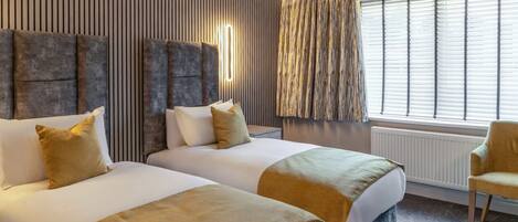 Ett hotellrum med två sängar, ett stort fönster med persienner, ett element och en stol.