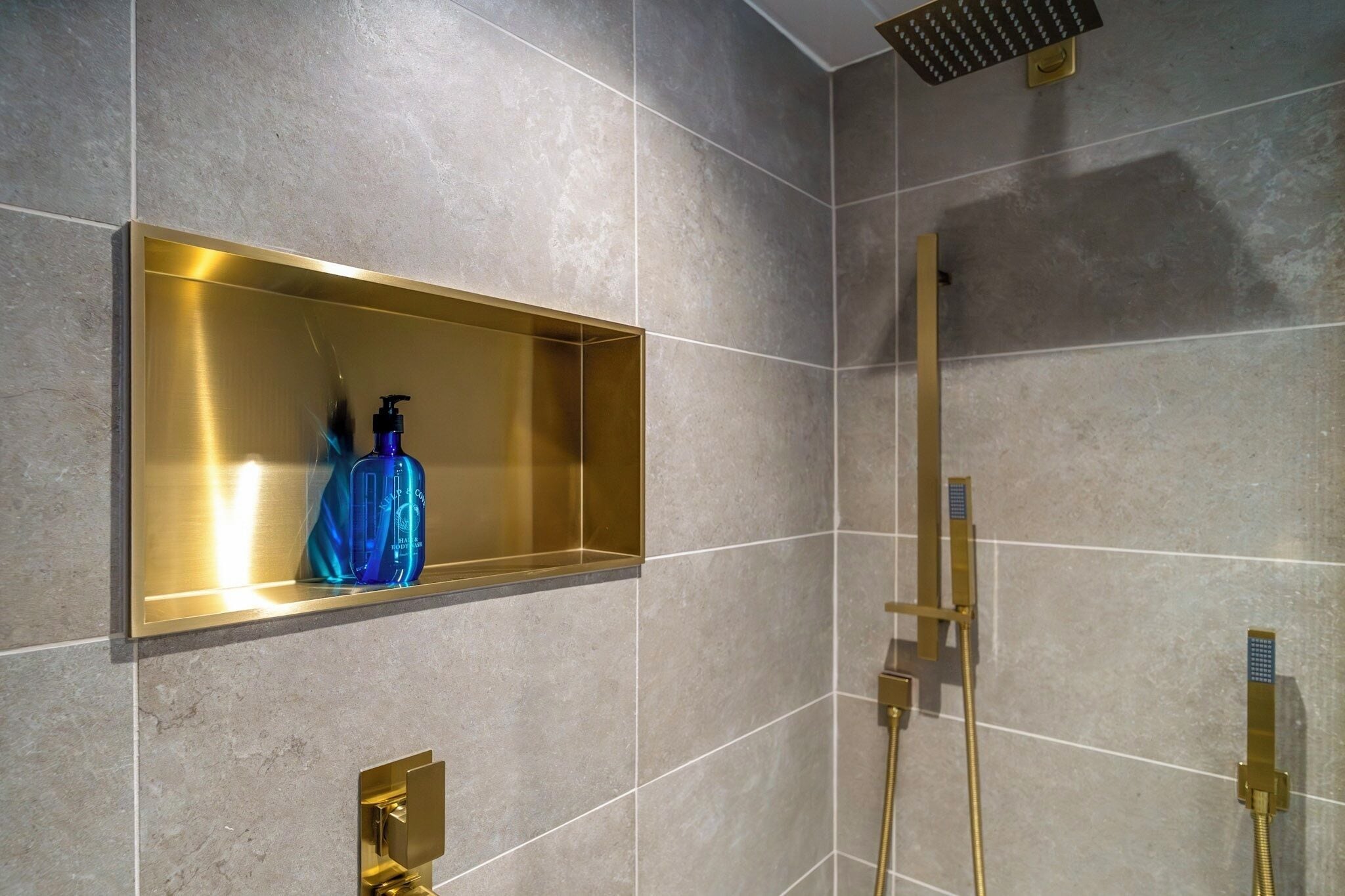 Un baño con un estante de marco dorado, una botella azul y un cabezal de ducha dorado.