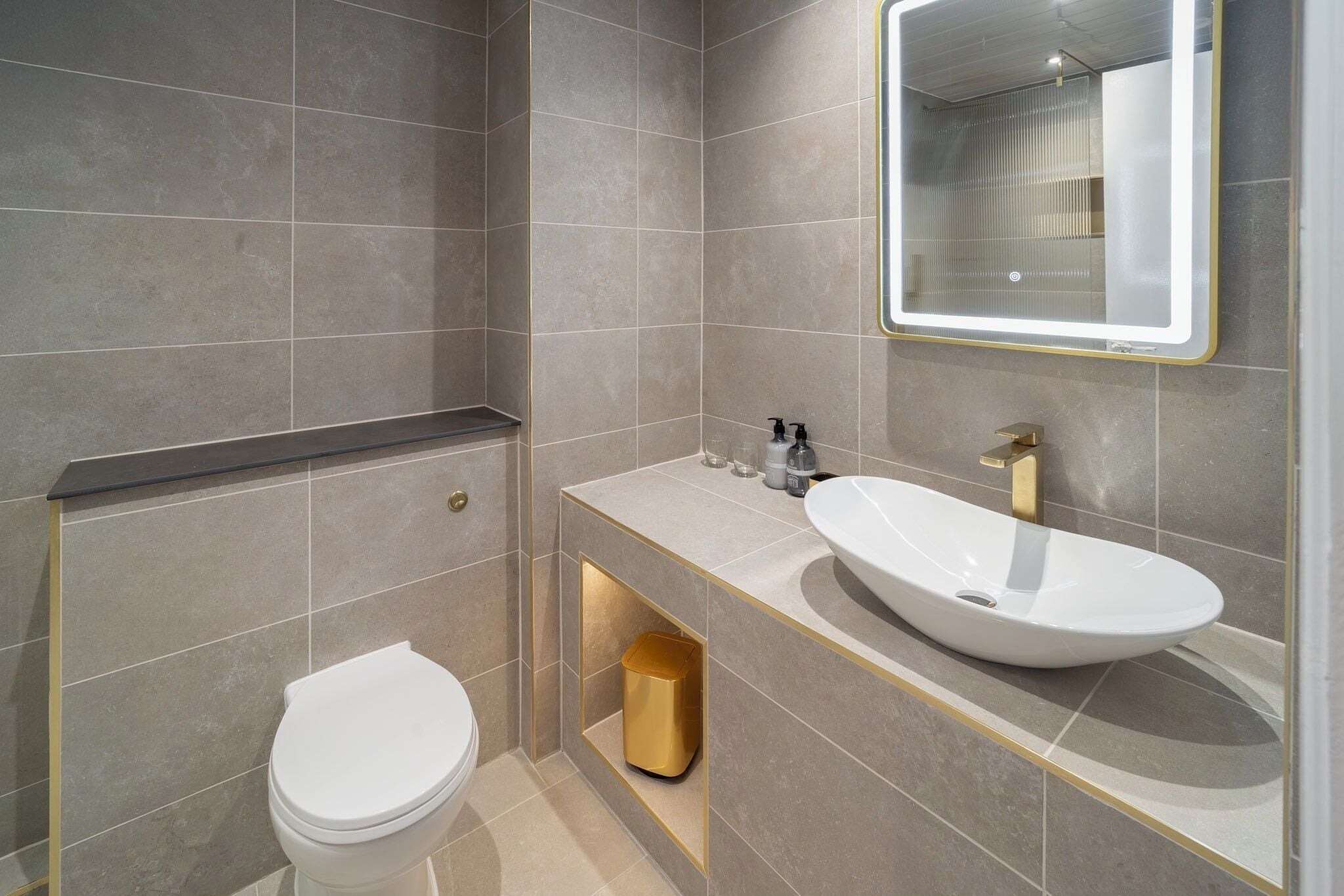 A bathroom with a white toilet, a sink with a gold faucet, and a mirror with a gold frame.