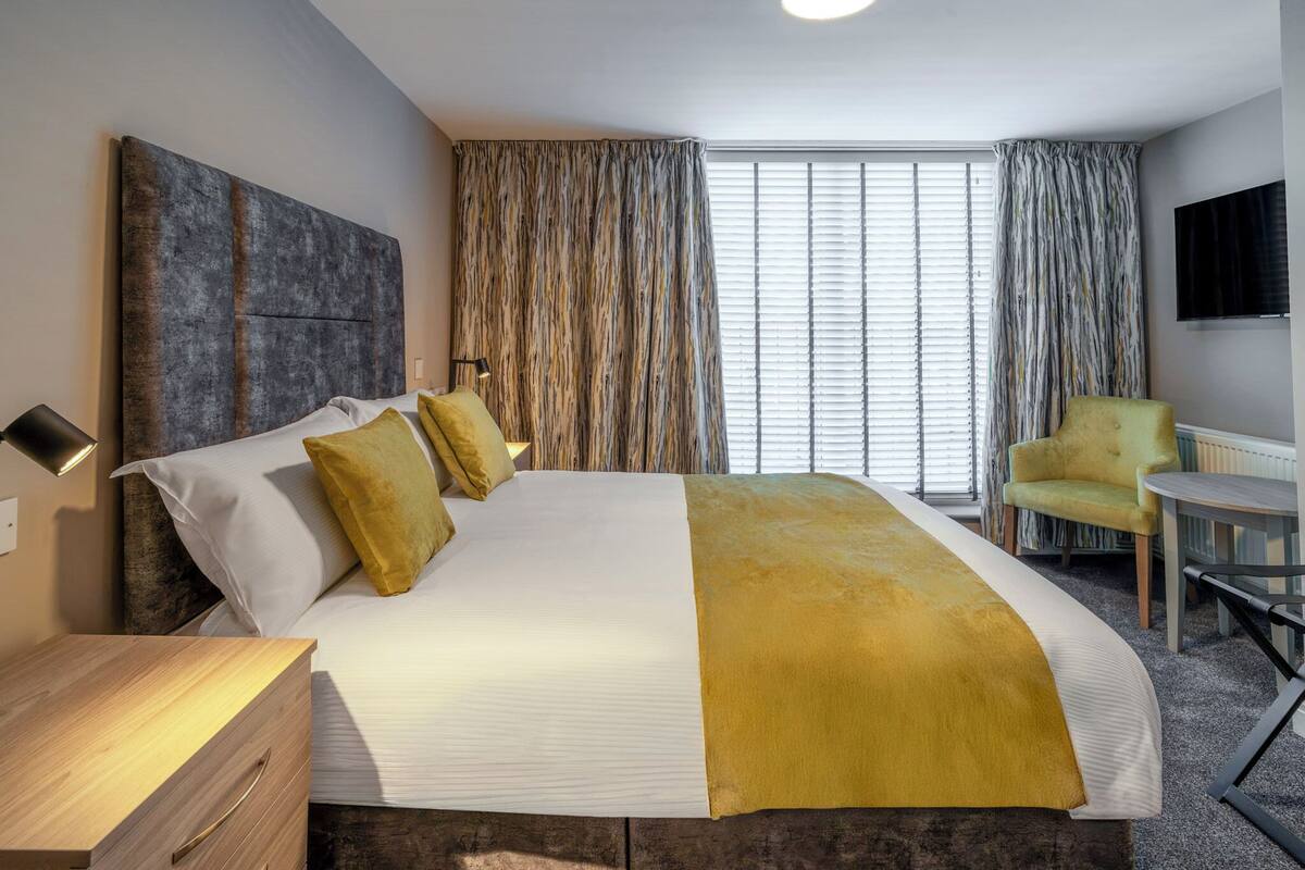 Une chambre d’hôtel avec un grand lit, une table de chevet, une chaise, une petite table et un téléviseur fixé au mur.