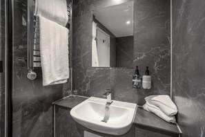 A bathroom with a marble sink, a towel rack, a mirror, and two bottles of toiletries. - Daresbury Park Hotel (Warrington)