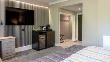 A modern bedroom with a bed, a TV, a small kitchenette, and a walk-in closet.