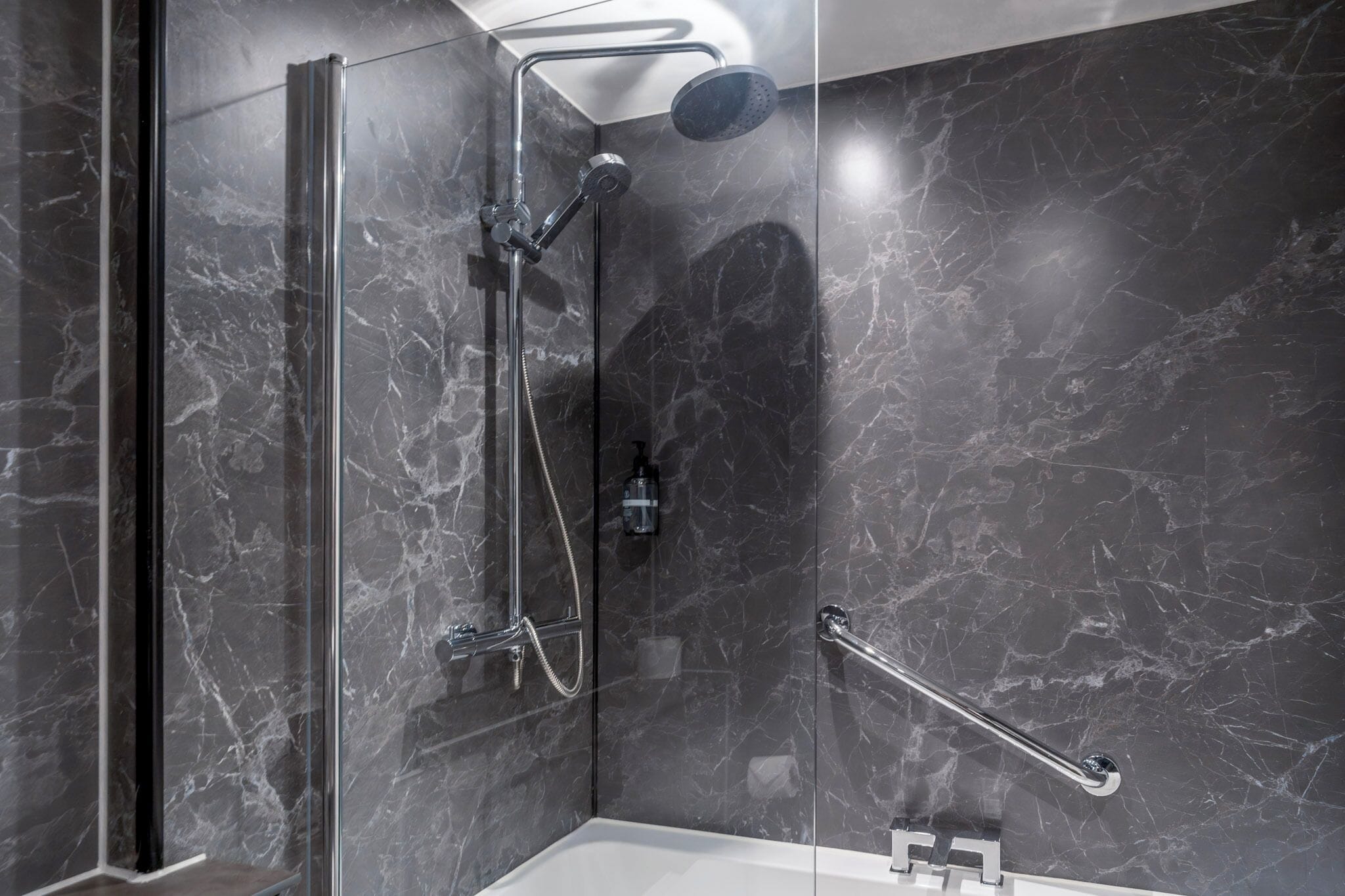 Un baño moderno con ducha de vidrio, paredes de mármol y barandilla.