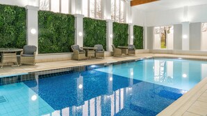 A swimming pool with a tiled edge, surrounded by wicker chairs and tables, and a wall with a green vertical garden.