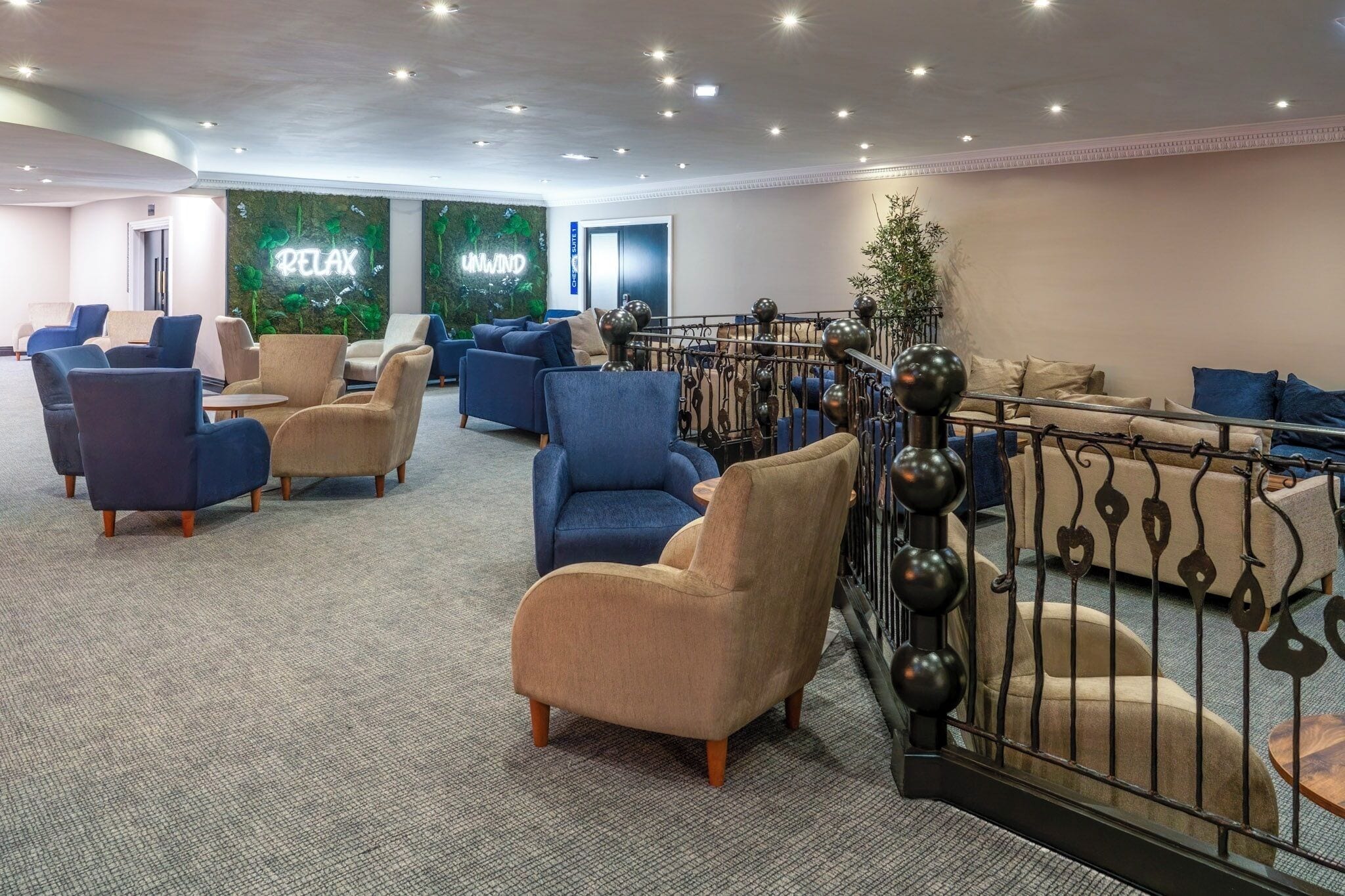 A modern lounge area with comfortable seating, a decorative wall with greenery, and a metal railing.