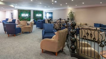 A modern lounge area with comfortable seating, a decorative wall with greenery, and a metal railing.