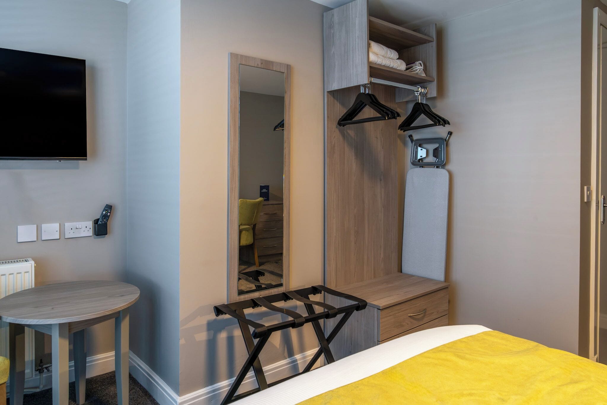 Habitació d'hotel amb llit, televisió penjada a la paret, mirall, taulell de fusta i taula petita.