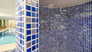 A bathroom with a blue mosaic tile wall, a shower area, and a pool visible in the background.