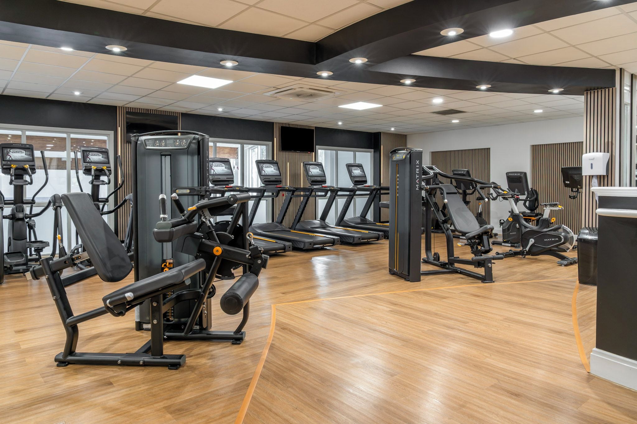 A gym with multiple treadmills, weight machines, and a wooden floor.
