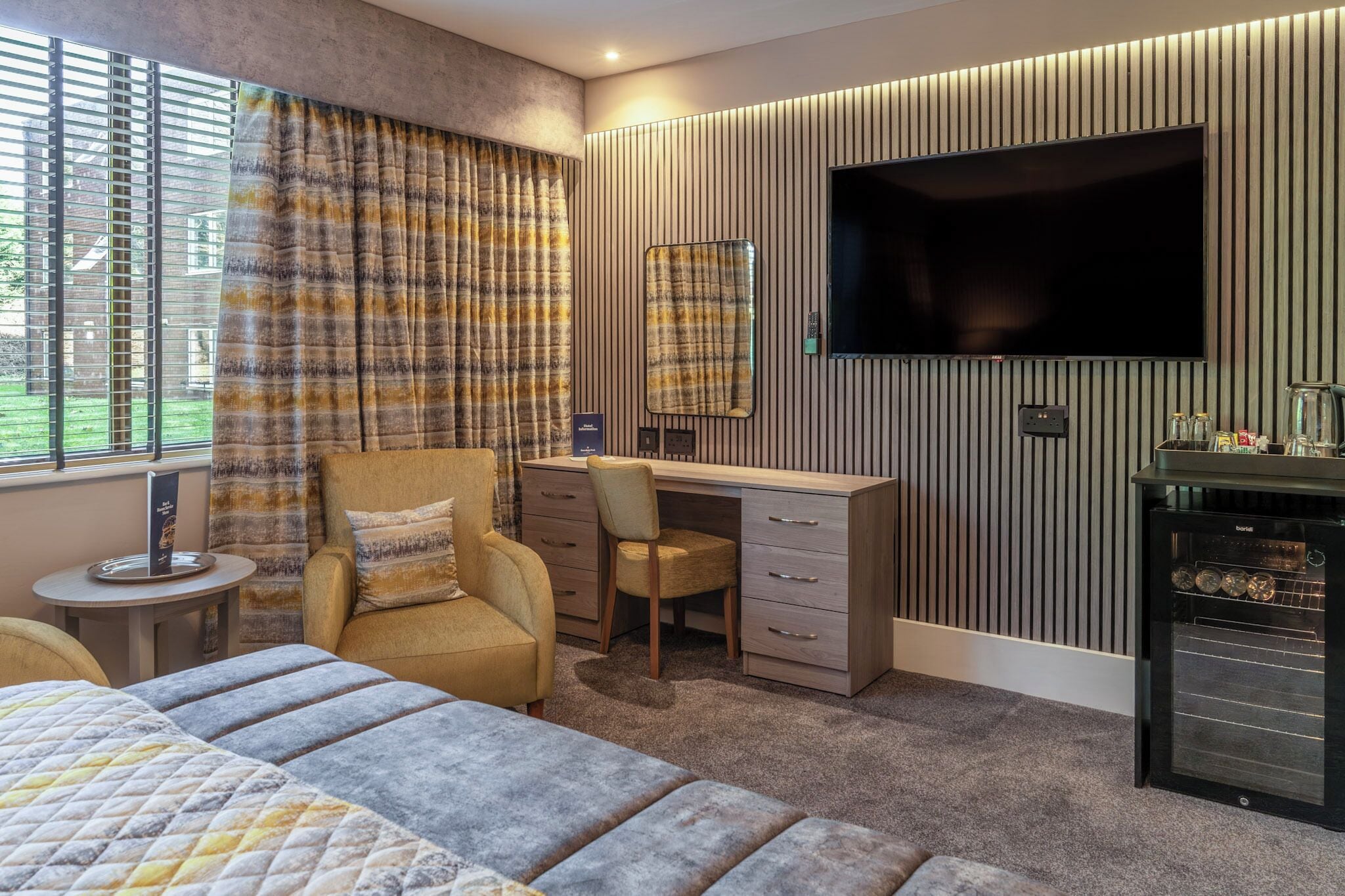 Ein Schlafzimmer mit Bett, Schreibtisch, Stuhl, Fernseher und einer Minibar.