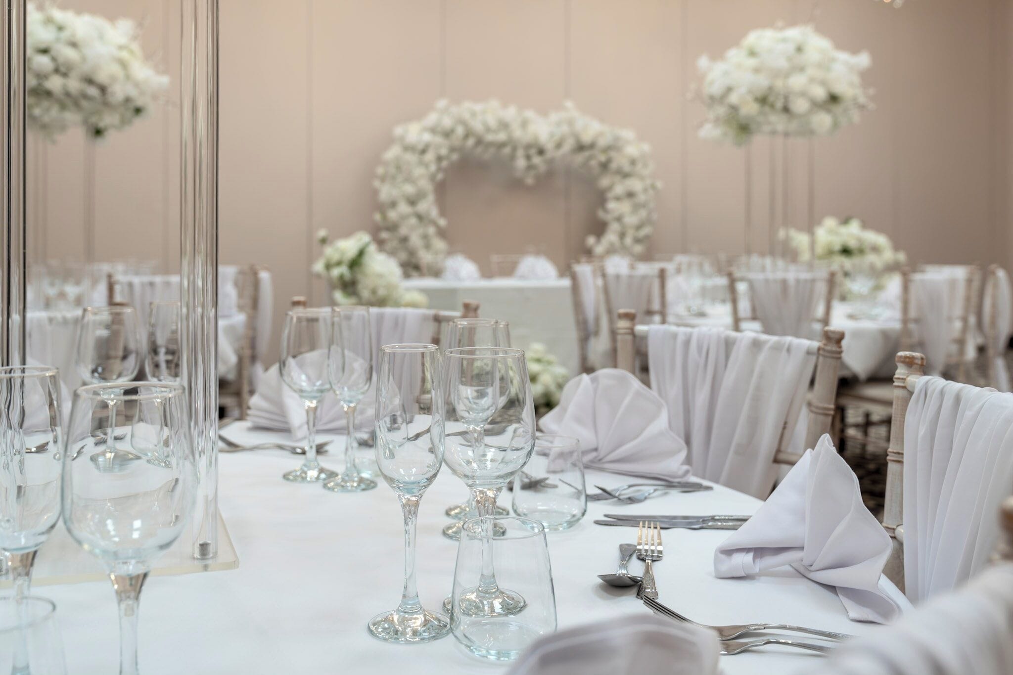 Un salón de banquetes con mesas redondas dispuestas para un evento formal, con copas de cristal transparente y manteles blancos.