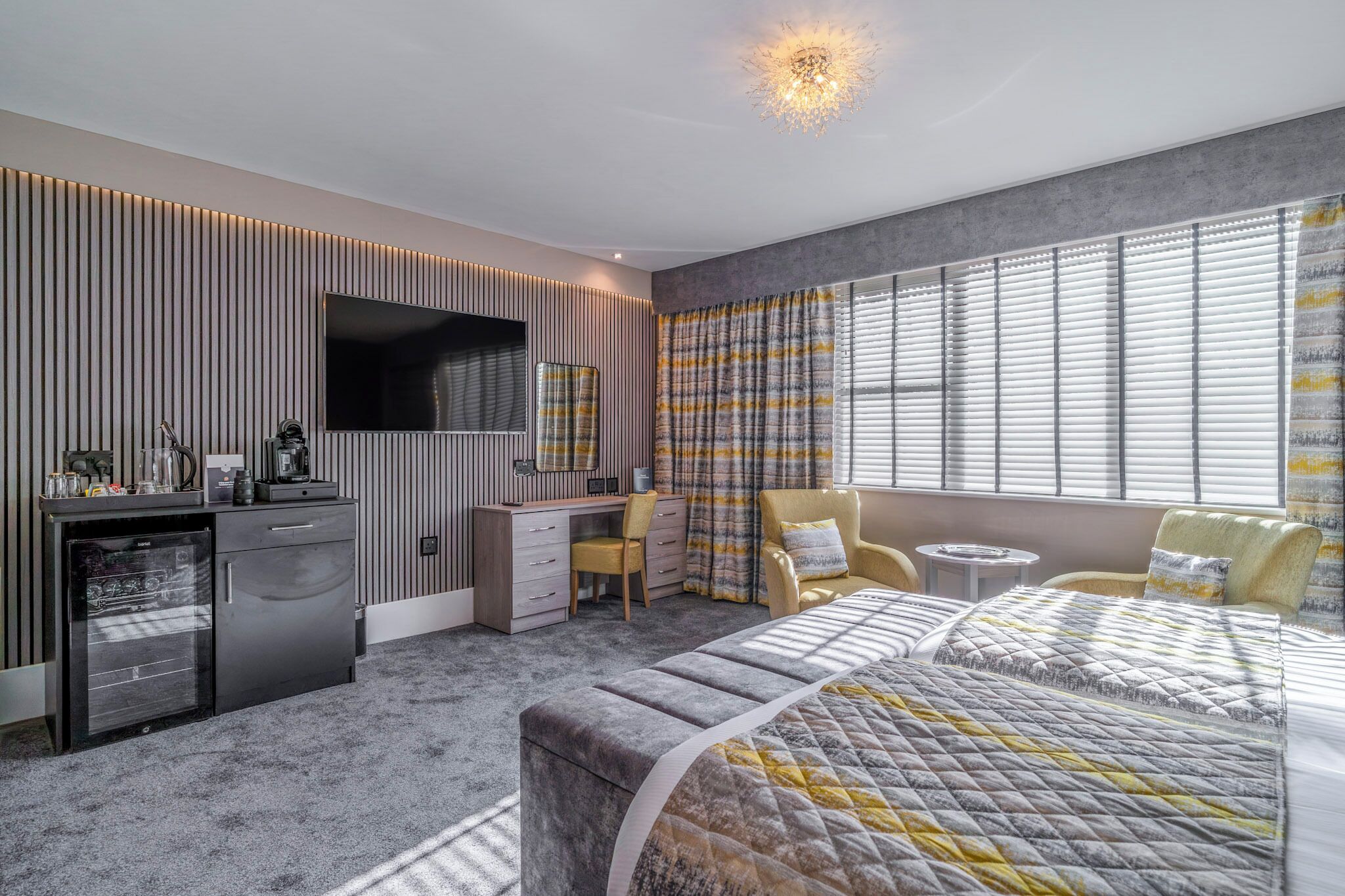 A modern bedroom with a bed, a desk, a TV, and a mini-fridge.