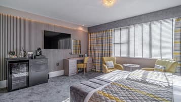 A modern bedroom with a bed, a desk, a TV, and a mini-fridge.