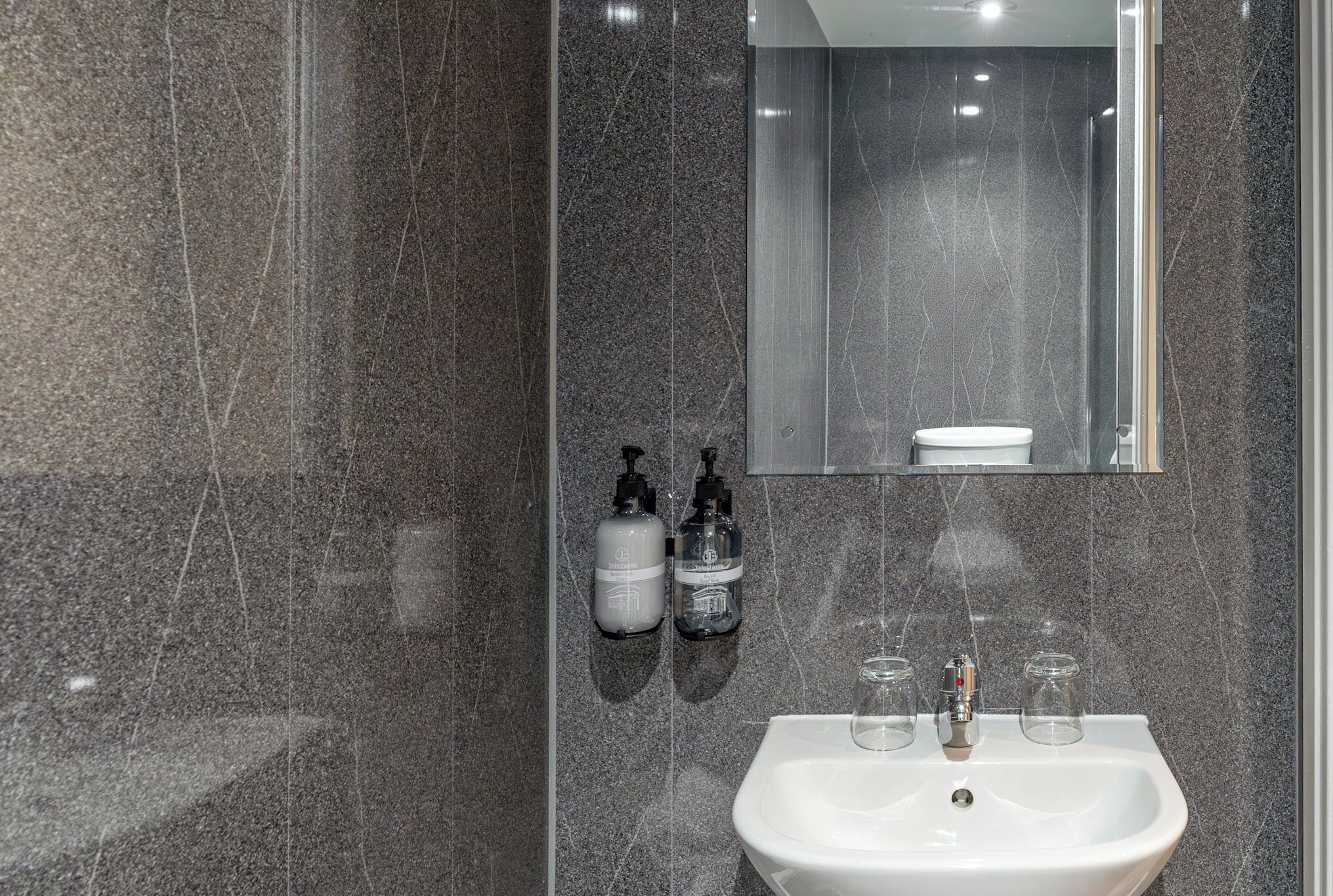 Une salle de bain avec un lavabo blanc, deux distributeurs de savon liquide et un miroir.