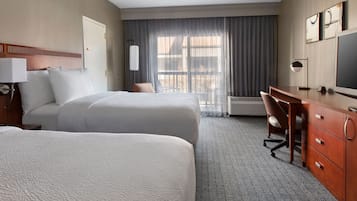 A hotel room with two beds, a desk, a chair, a television, and a window with curtains.
