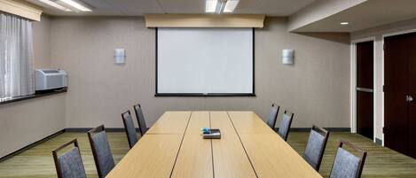 A conference room with a long table, chairs, a projector screen, and an air conditioning unit.