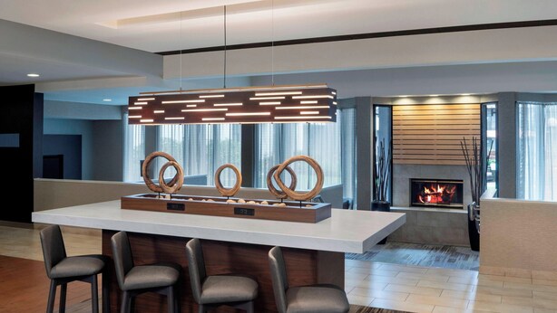 A modern kitchen with a central island, bar stools, a fireplace, and a contemporary pendant light.