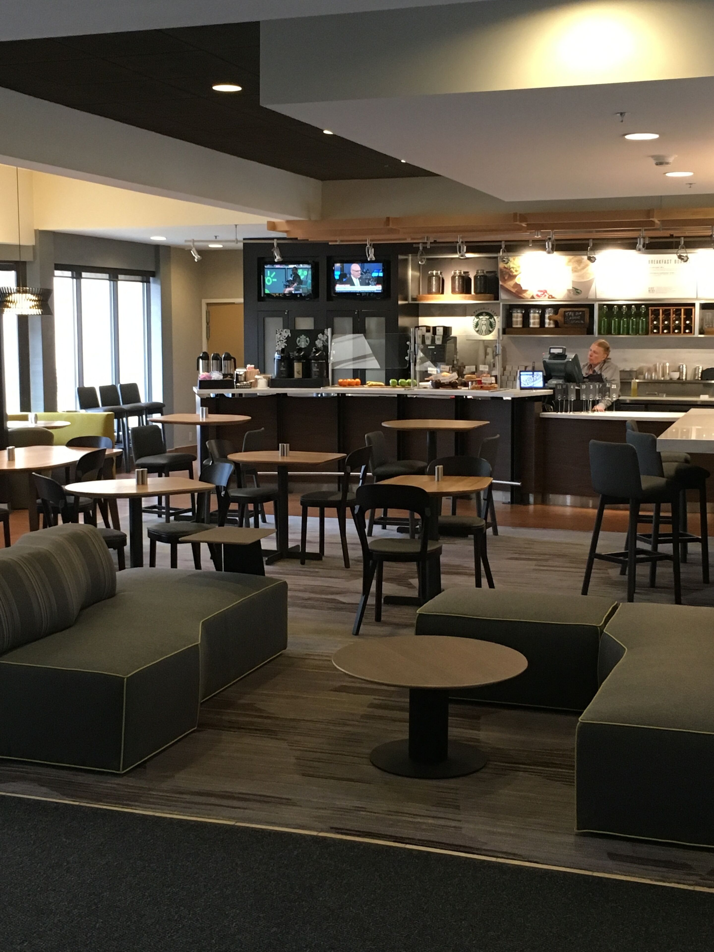 A modern hotel lobby with a bar area, seating arrangements, and a television screen.