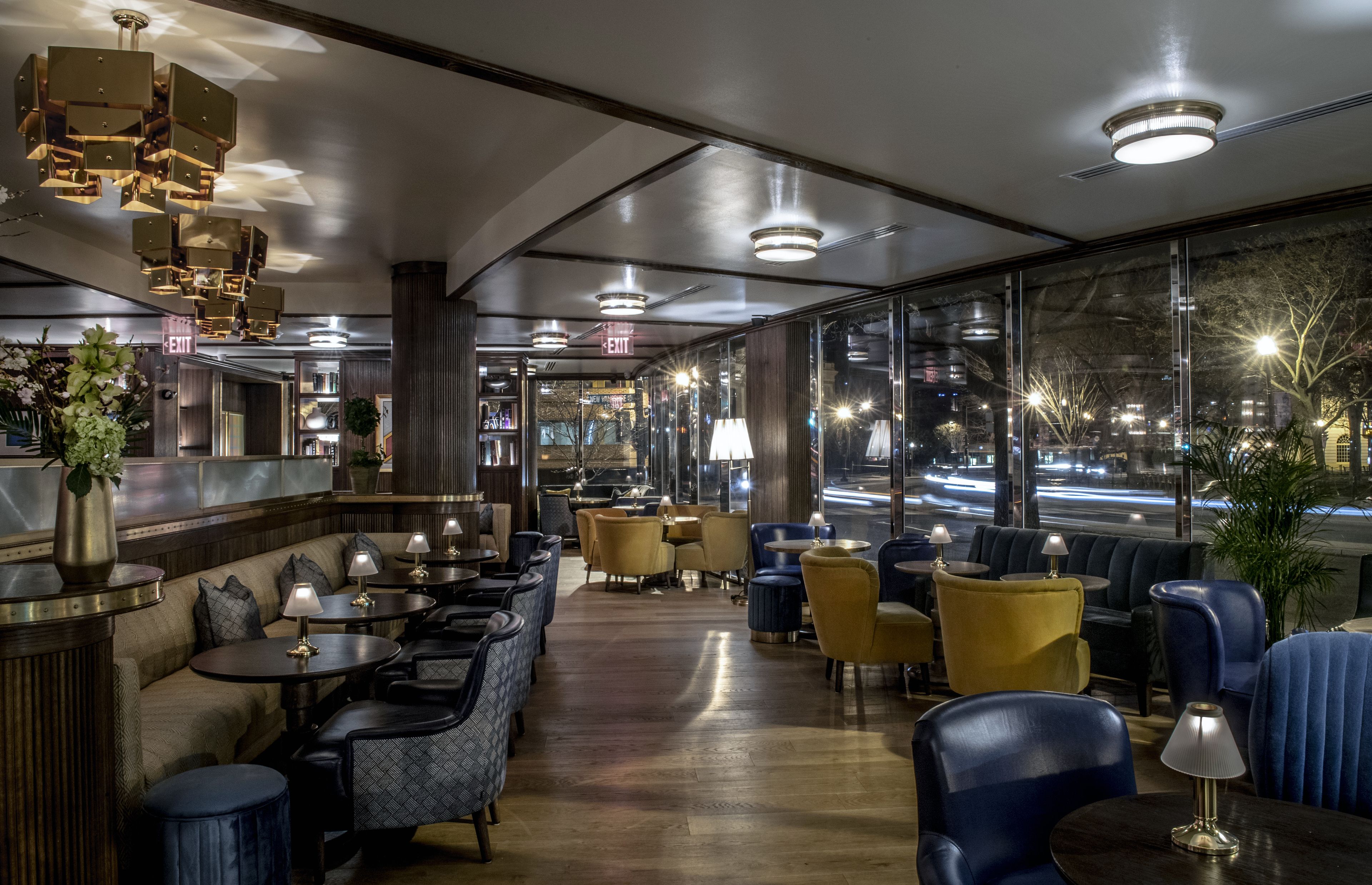 A modern restaurant with a bar area, seating with tables and chairs, and large windows offering a city view.