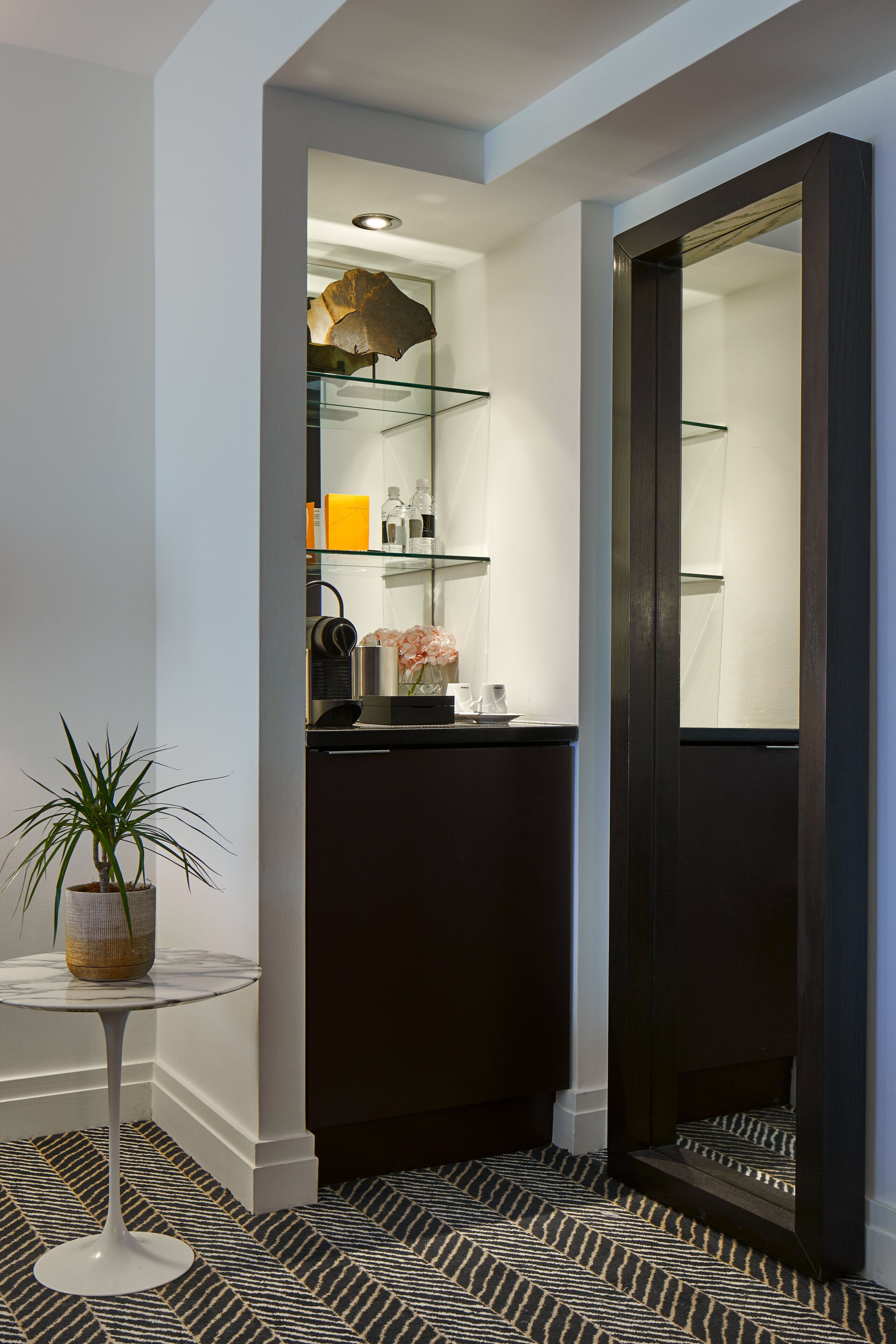 A modern bathroom with a glass shower enclosure, a potted plant, and a patterned floor.