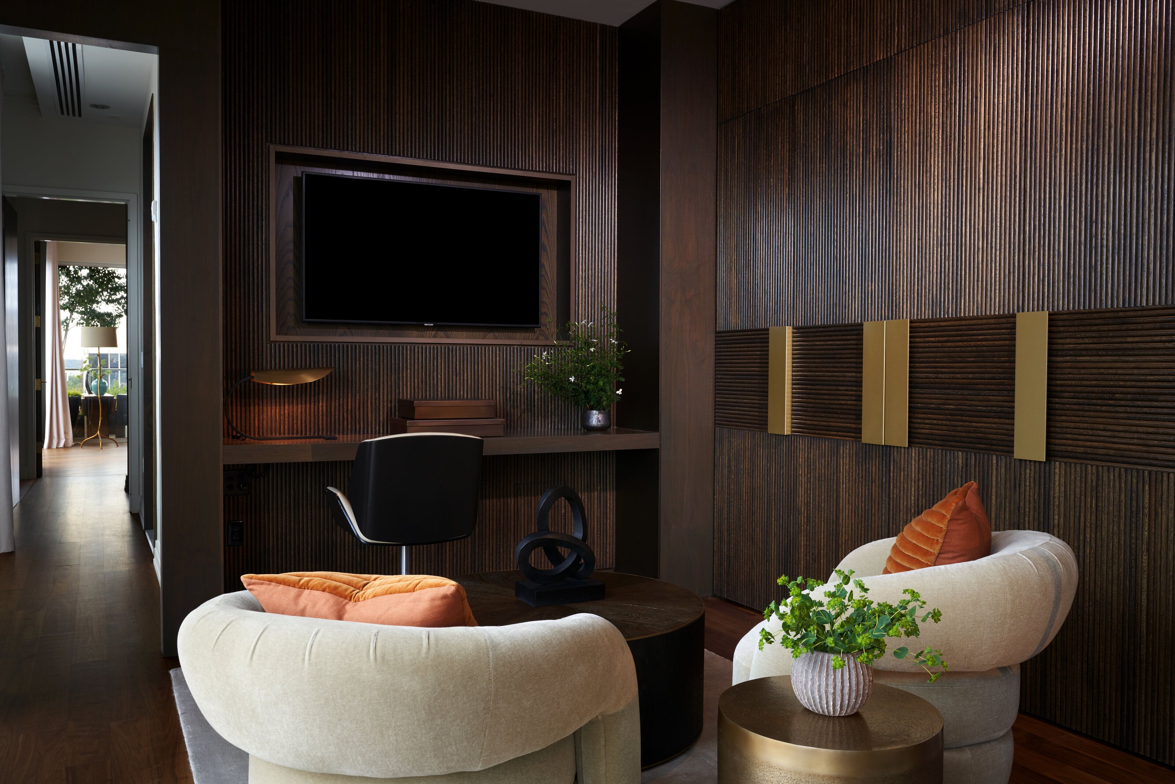A modern living room with a flat-screen TV mounted on a wooden wall, a round coffee table, two sofas with cushions, and a small side table with a plant.