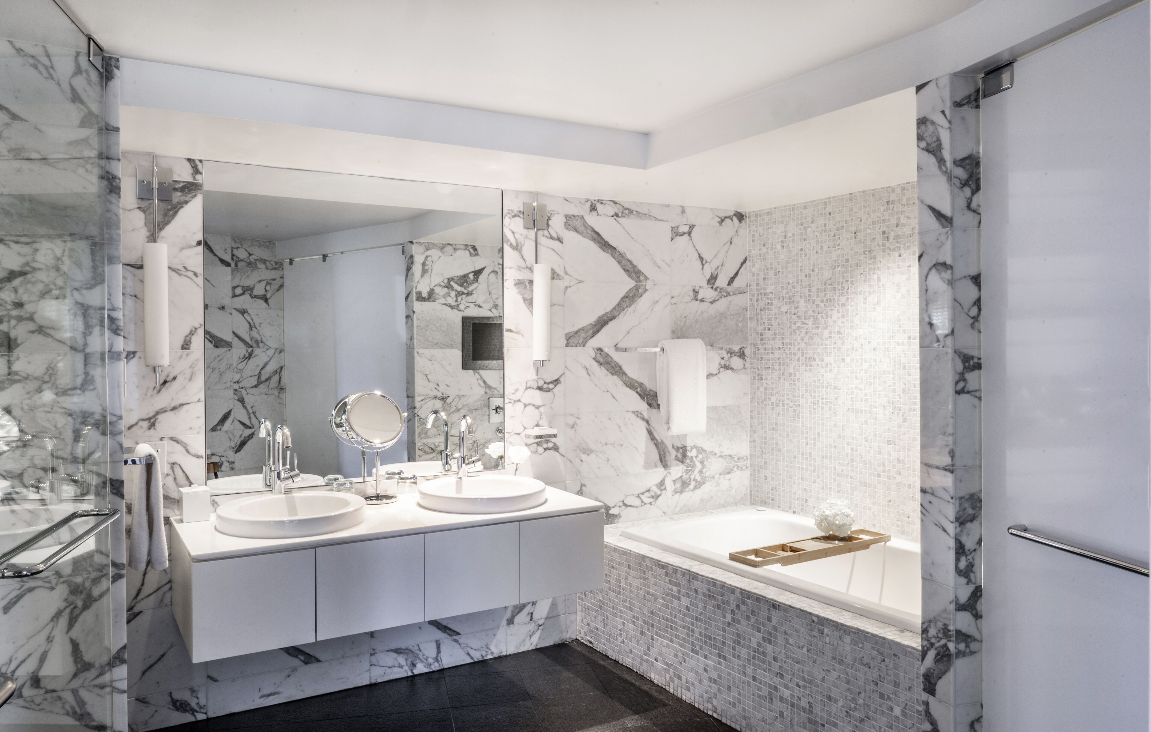 A modern bathroom with two sinks, a large mirror, and a bathtub.