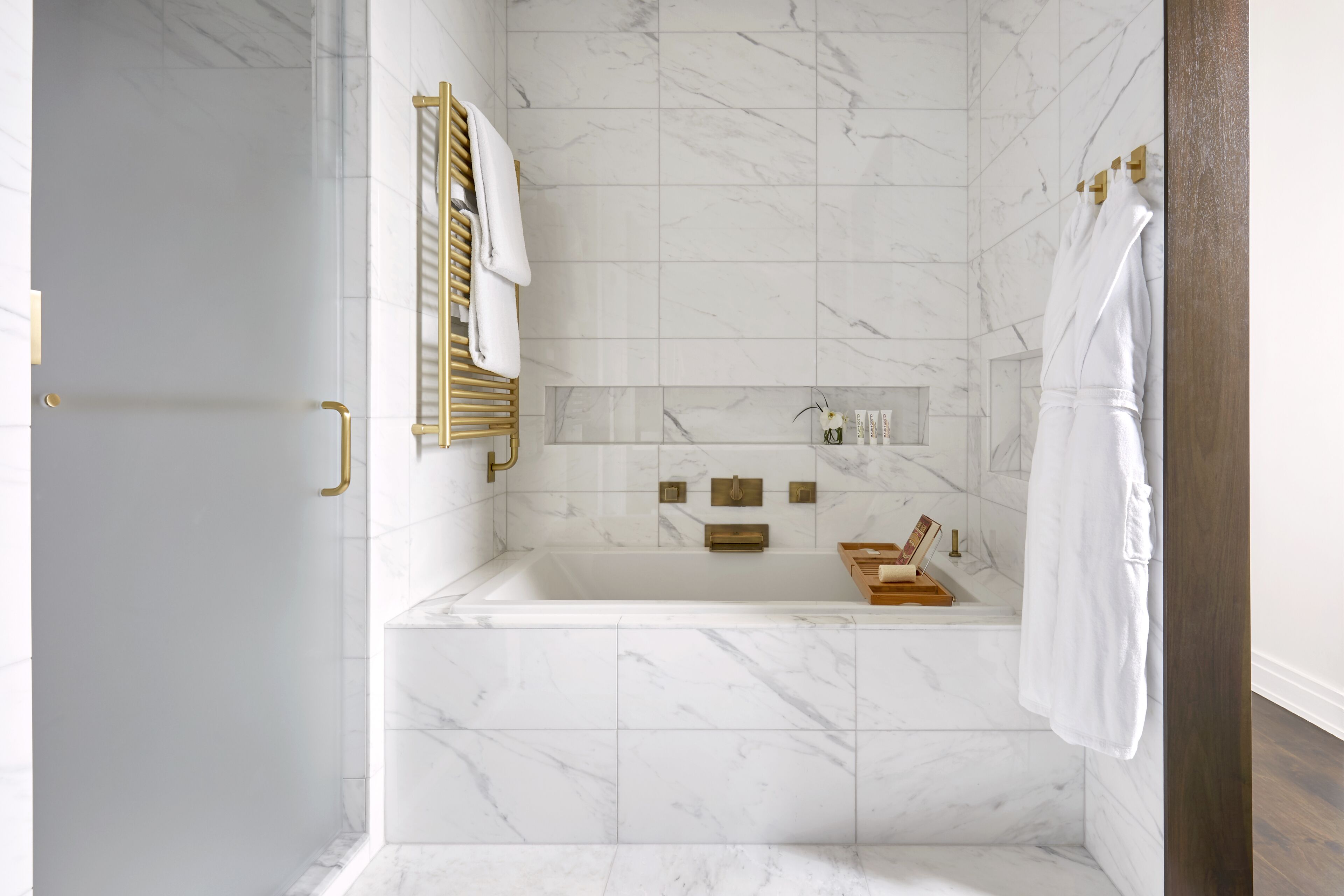 A modern bathroom with a marble floor, a freestanding bathtub, and gold fixtures.
