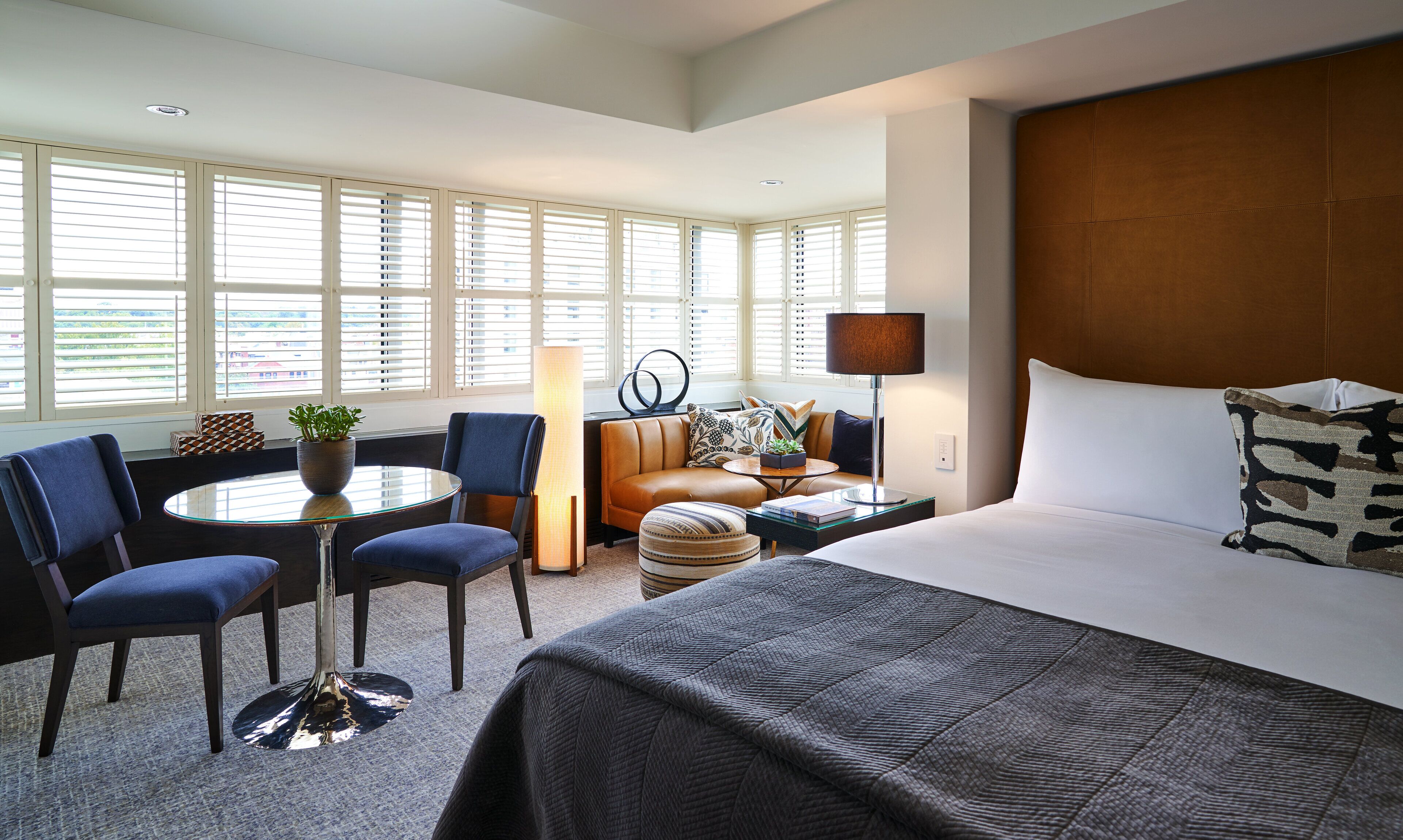 A hotel room with a large bed, a seating area with a table and chairs, a lamp, and a view through the window.