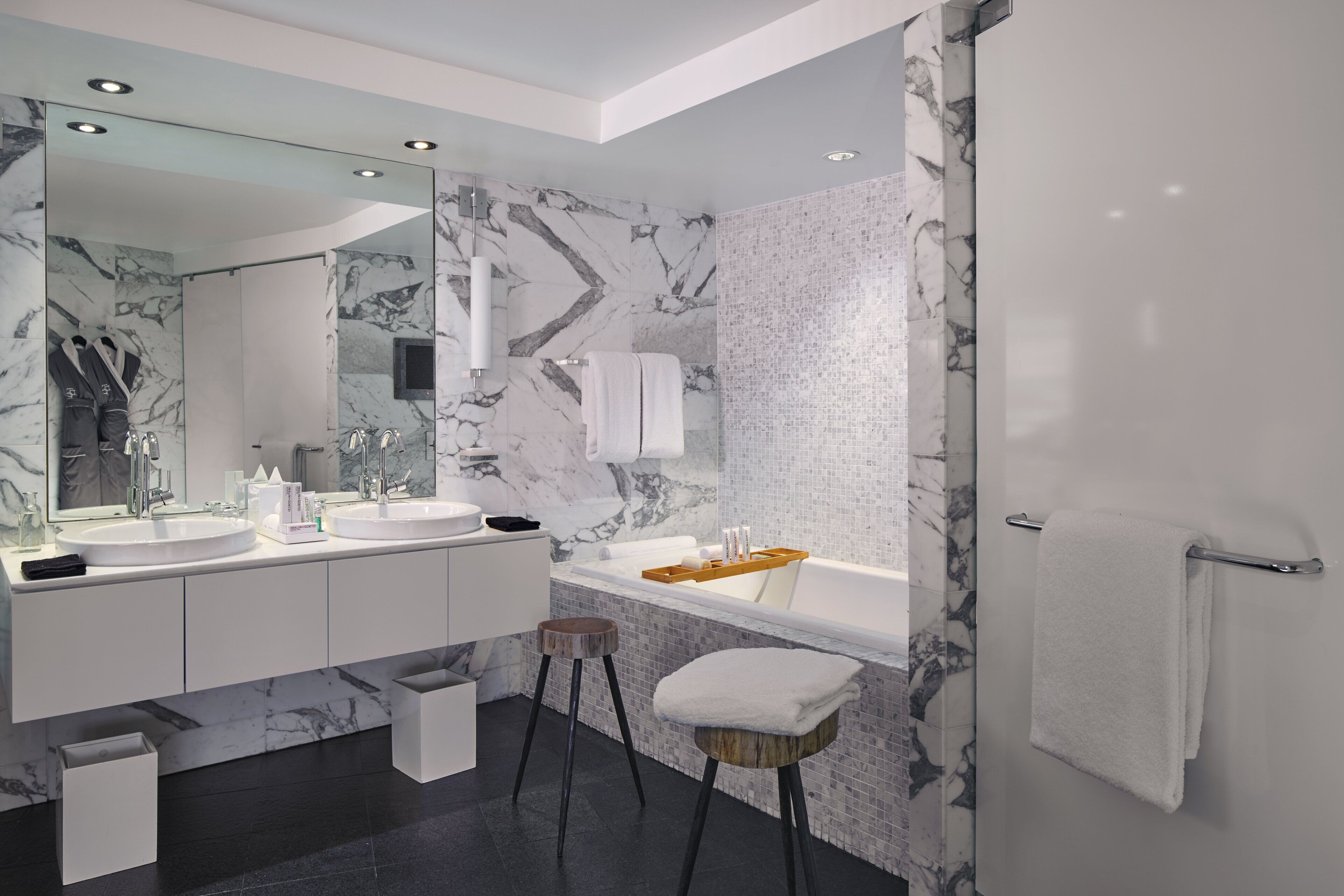 A modern bathroom with two sinks, a large mirror, and a bathtub.
