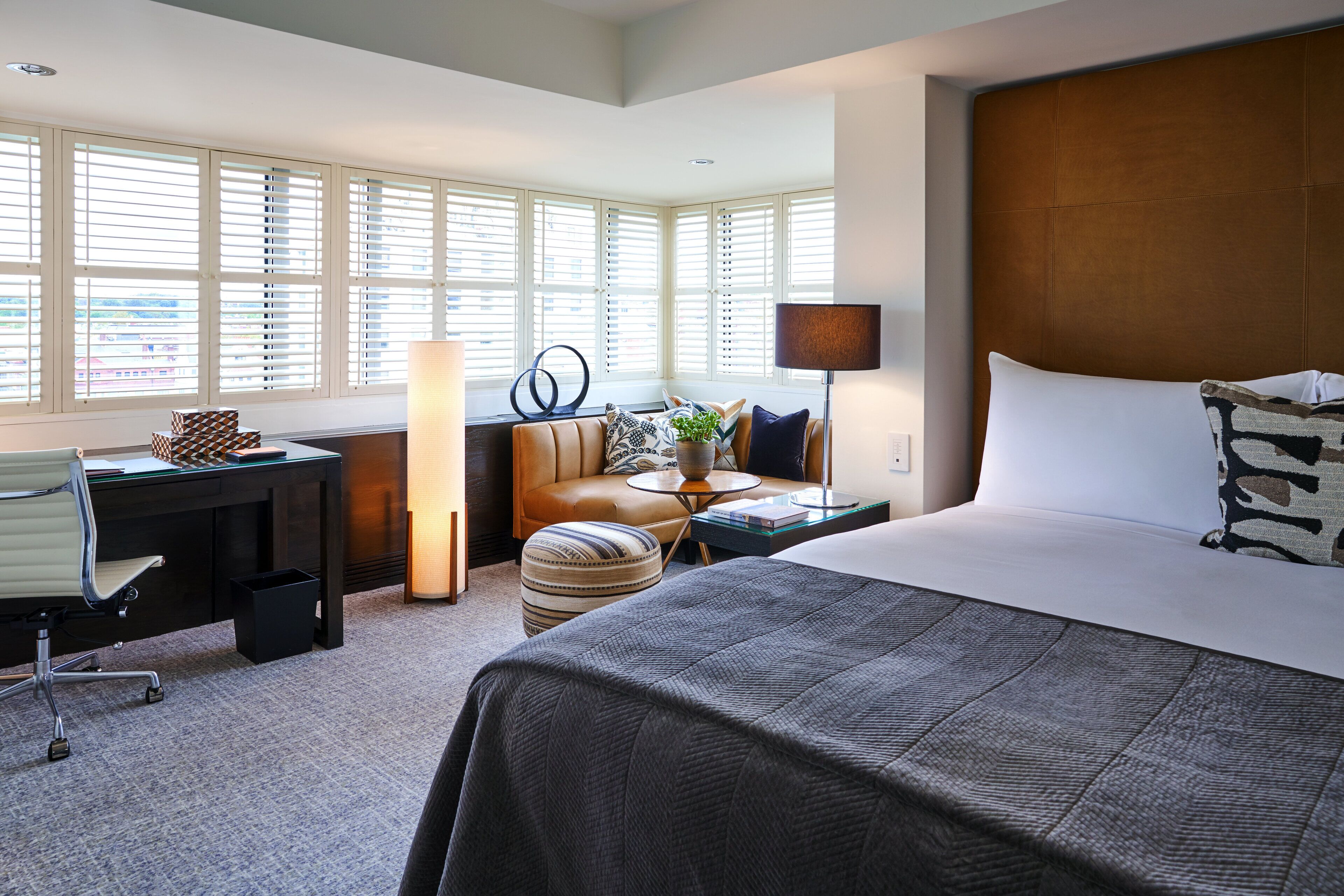 Une chambre d’hôtel avec un grand lit, un bureau, une chaise, un canapé et une fenêtre avec des stores.